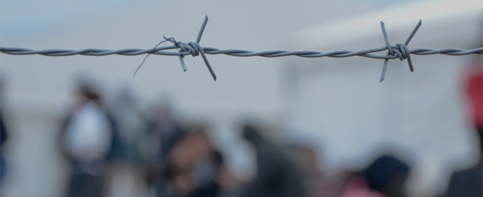Barbed wire fence with people in the background, representing migration and border enforcement