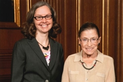 [ai] Two women standing together in a formal setting. One woman has curly hair and glasses, wearing a black blazer. The other woman, with a short hairstyle, is in a beige sweater and is wearing glasses, both smiling in front of a wooden backdrop.