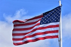 [ai] The United States flag waving against a blue sky, displaying red and white stripes along with a blue field featuring white stars.