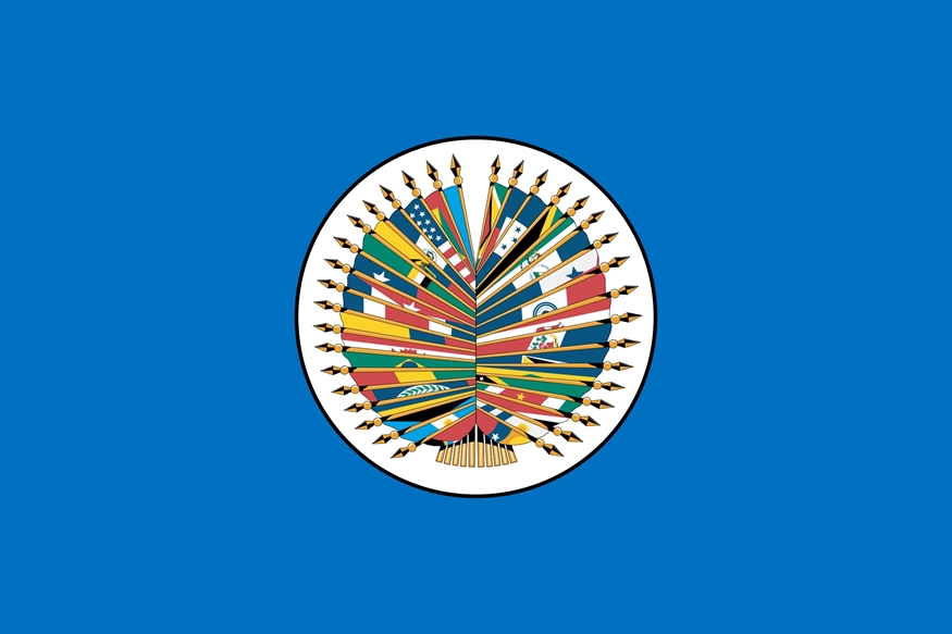 [ai] The flag of the Organization of American States (OAS) featuring a central emblem of eighteen colored flags arranged in a circular pattern, surrounded by blue background.