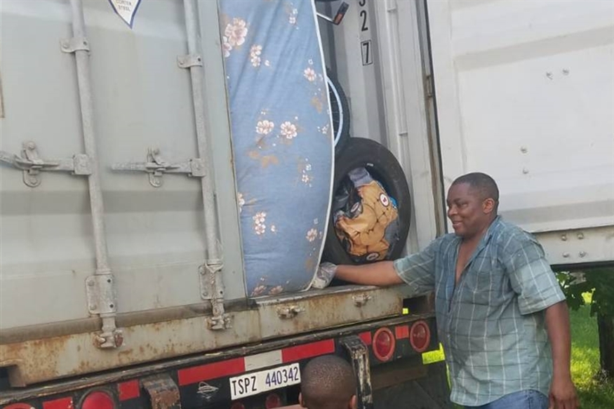 [ai] Two men unloading items from the back of a truck. One man is holding onto a mattress, while the other is reaching in to retrieve an object.
